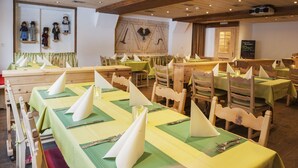 A restaurant with wooden tables and chairs, green tablecloths, and white napkins. - Hotel Tenne (Saas-Fee)