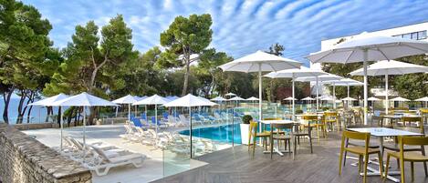A poolside area with lounge chairs and umbrellas, a pool, and dining tables and chairs.