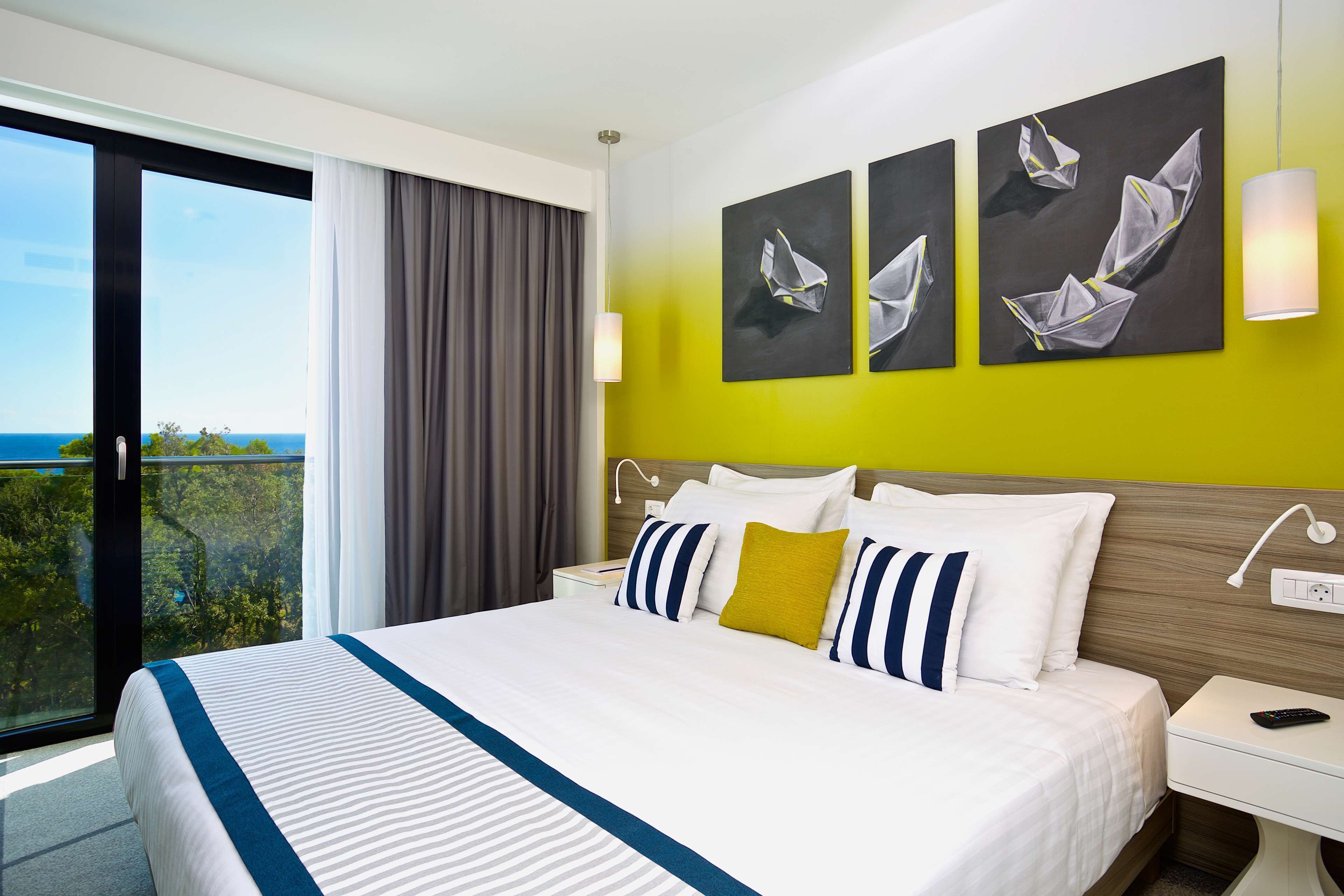 A hotel room with a large bed, a nightstand, a lamp, and artwork on the wall.