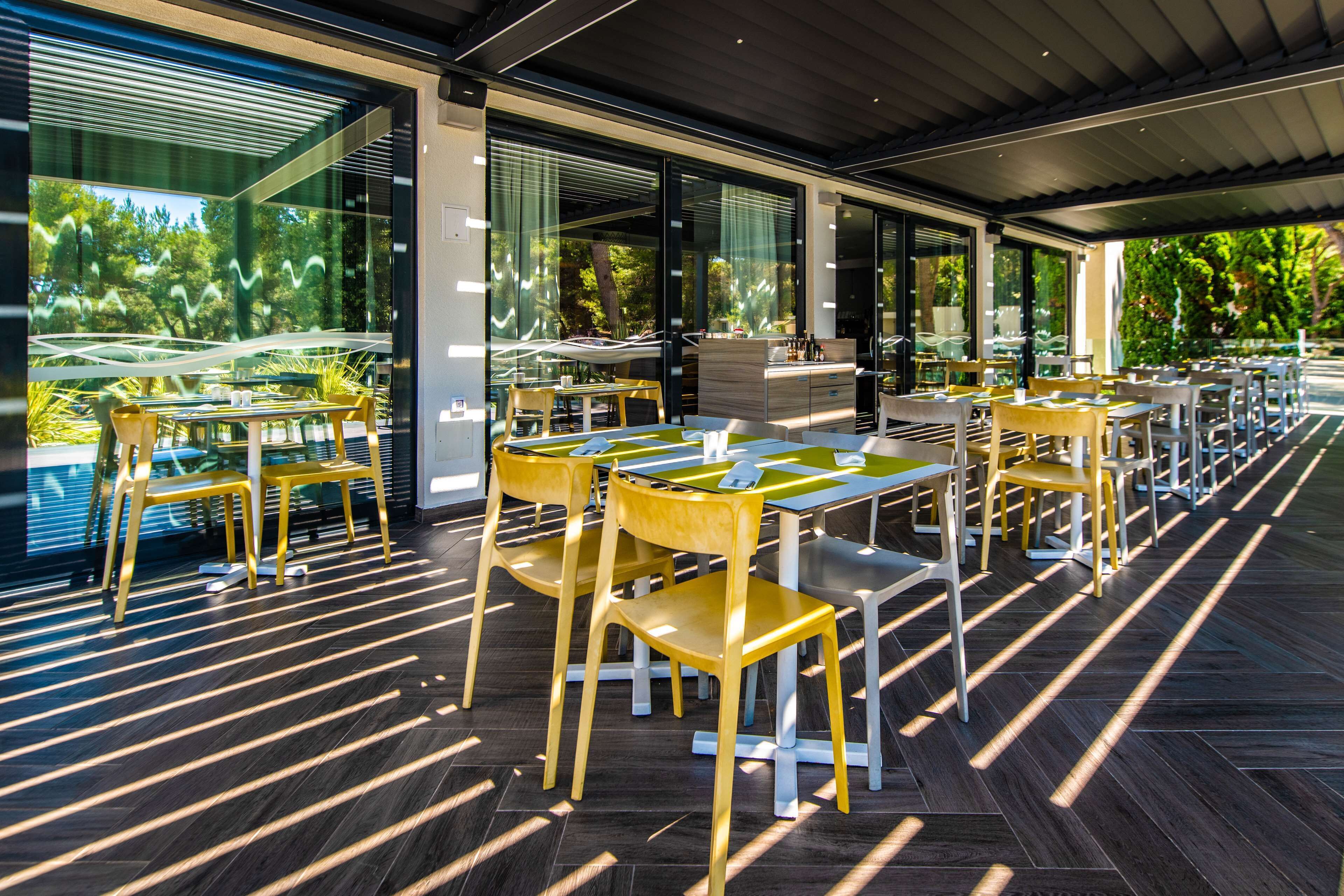 An outdoor dining area with modern furniture and large windows overlooking a garden.
