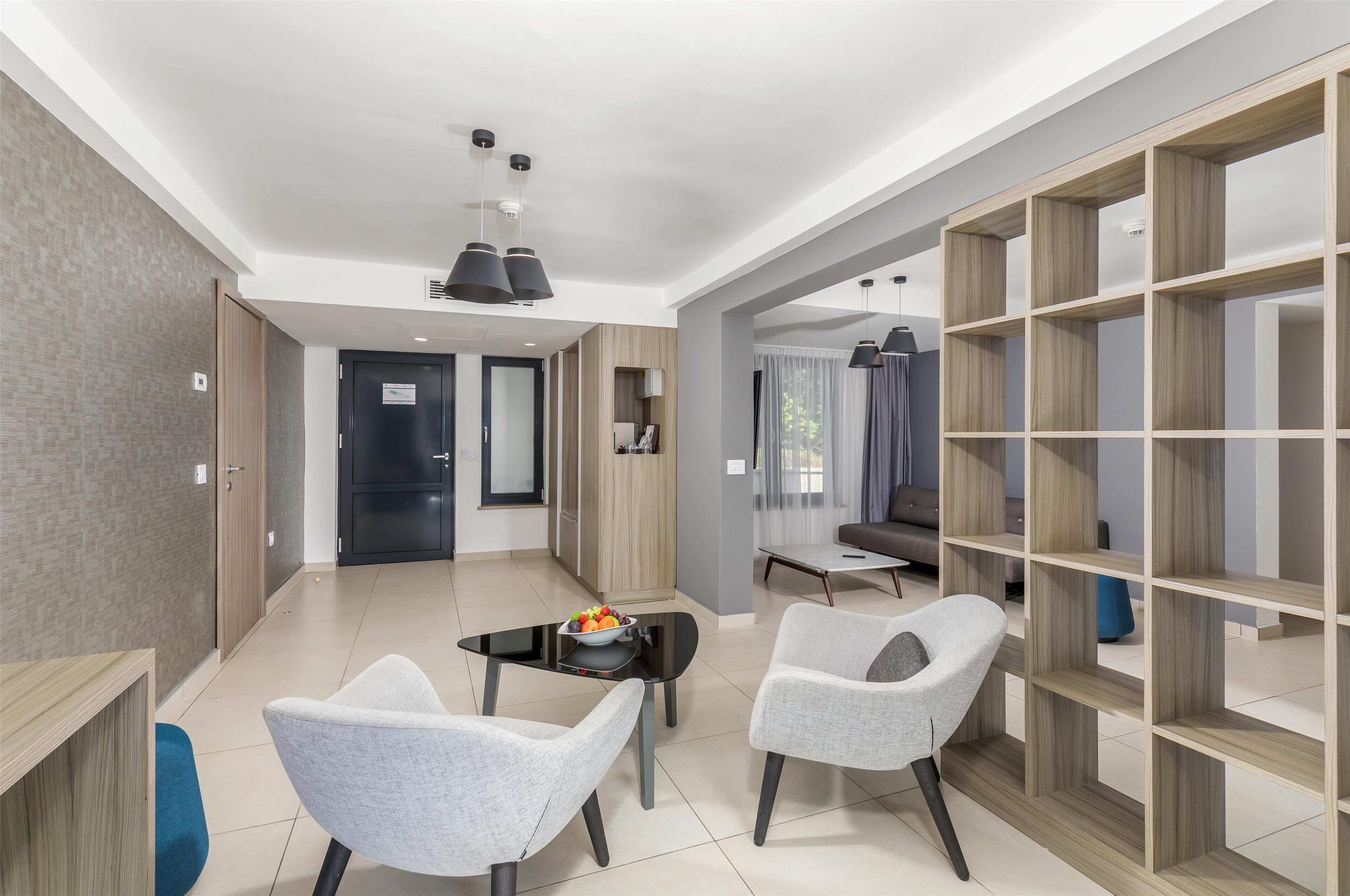 A modern hotel room with a dining area, a seating arrangement, and a large wooden shelving unit.