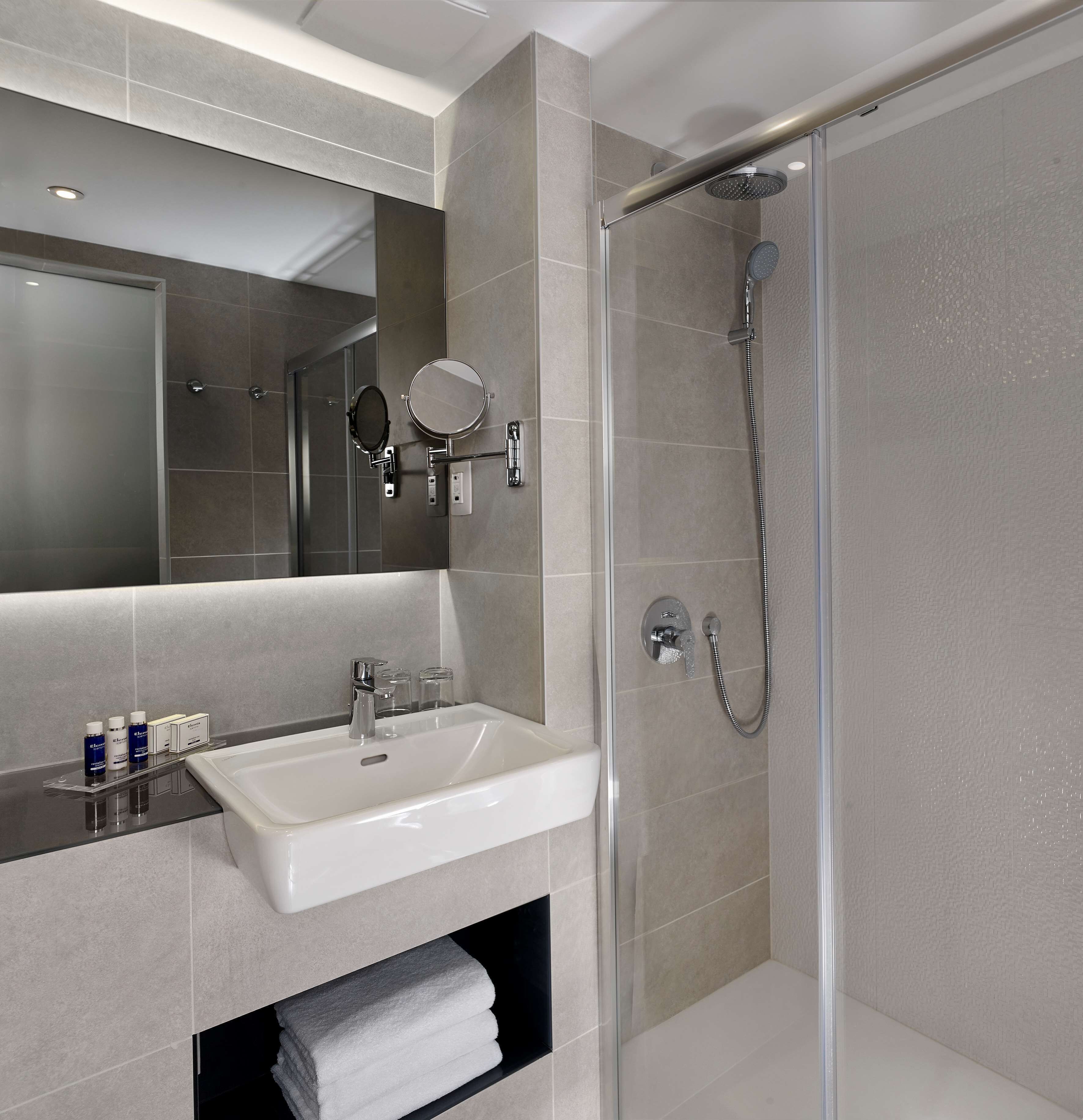 Een moderne badkamer met een glazen douchecabine, een witte wastafel en een spiegel.