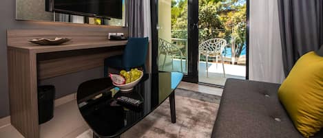 A modern living room with a flat-screen TV, a dining area with a bowl of fruit, and a sofa with a yellow pillow.