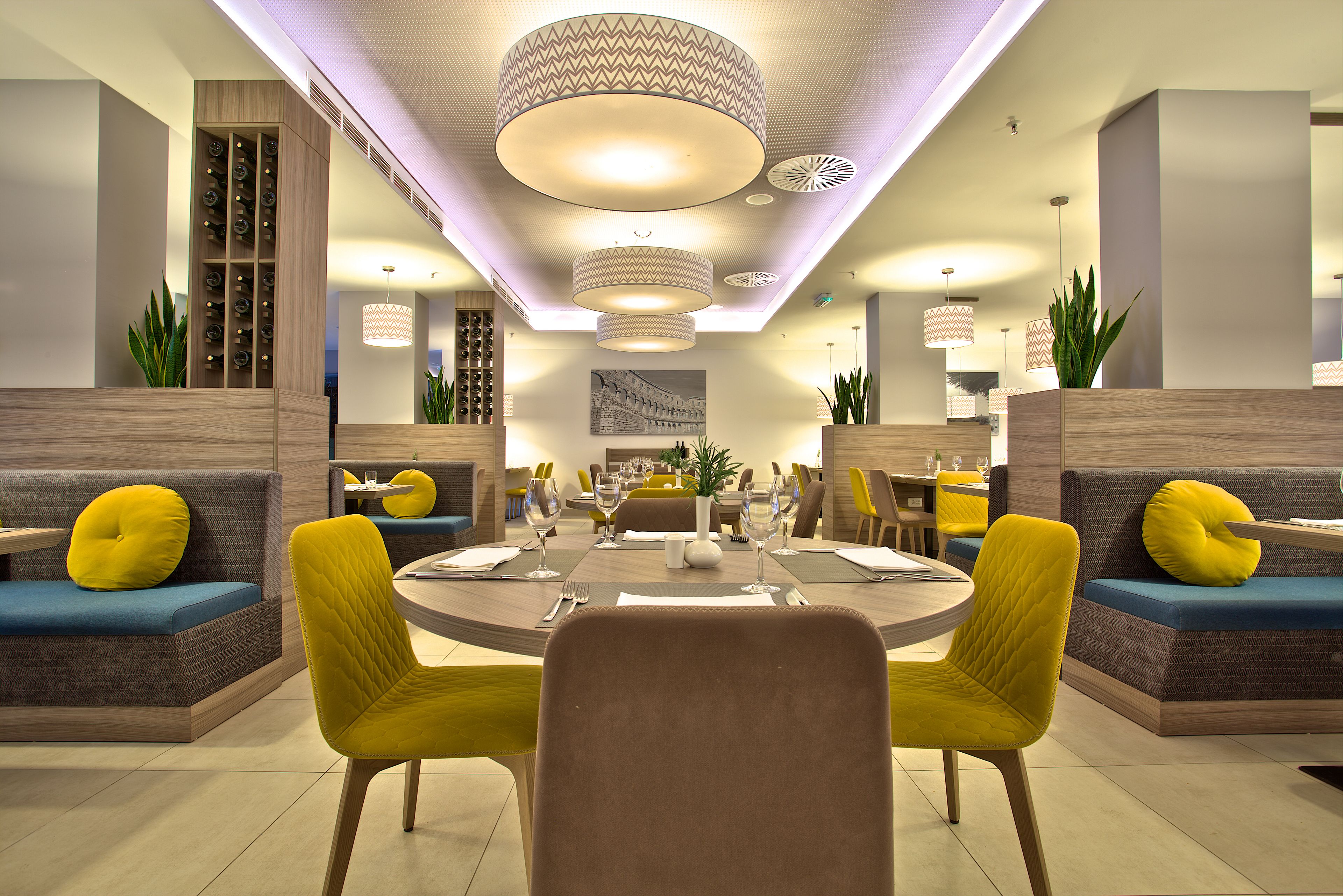 A modern dining area with round tables, yellow chairs, and a central seating area with sofas and cushions.