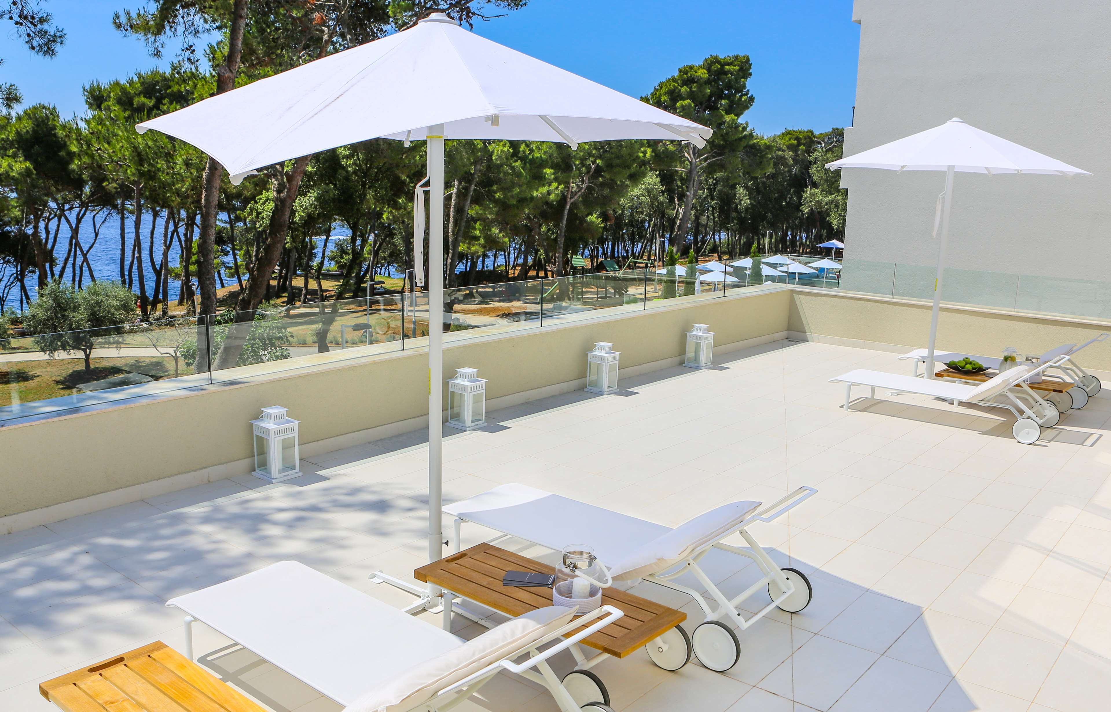 Eine sonnendurchflutete Außenpatio mit Liegestühlen, weißen Sonnenschirmen und Blick auf das Meer.