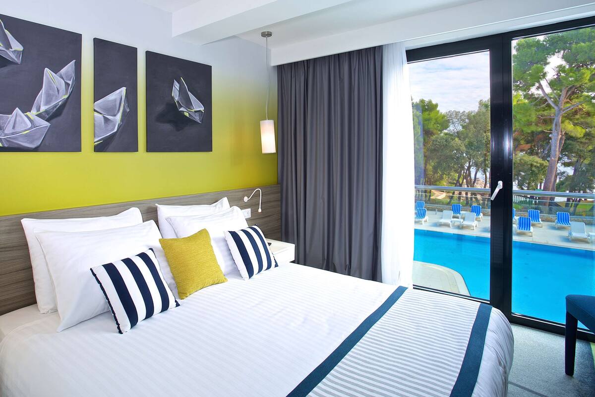 Quarto de hotel com uma cama grande, vista para uma piscina e obras de arte na parede.