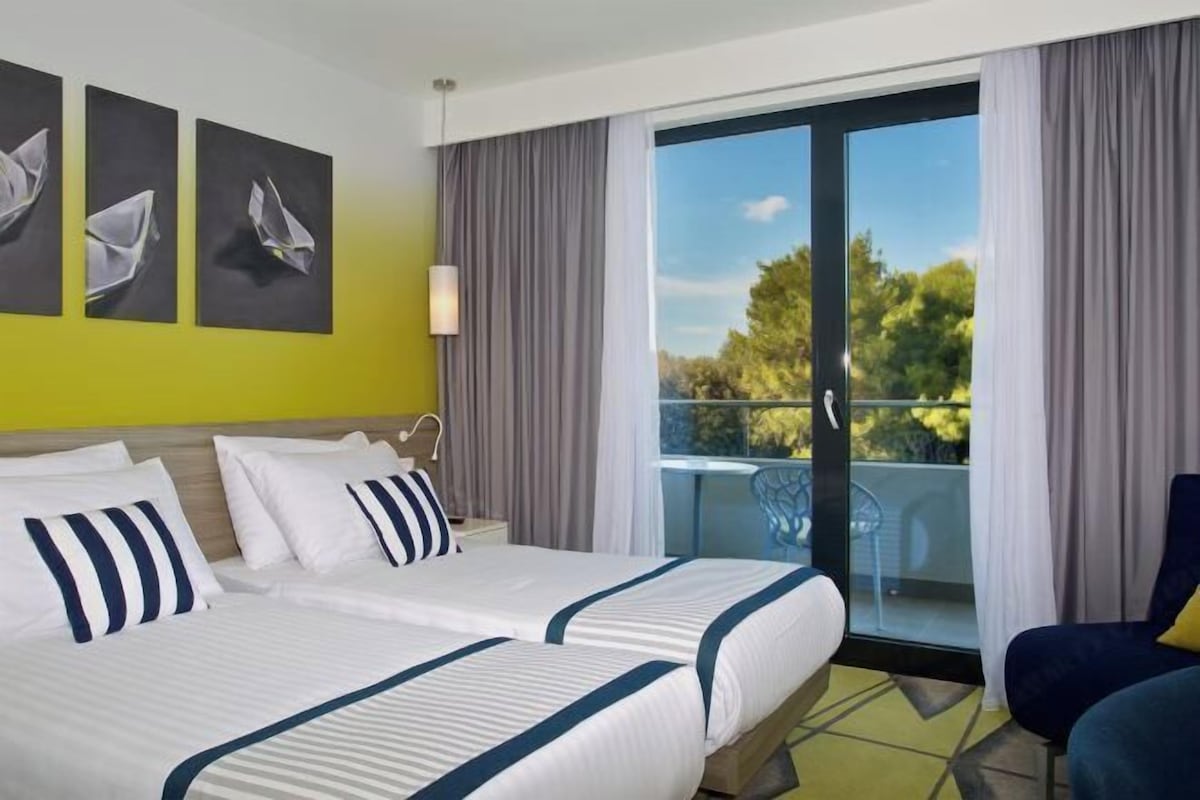 Ein Hotelzimmer mit zwei Betten, einem Balkon mit Blick und Bildern an der Wand.