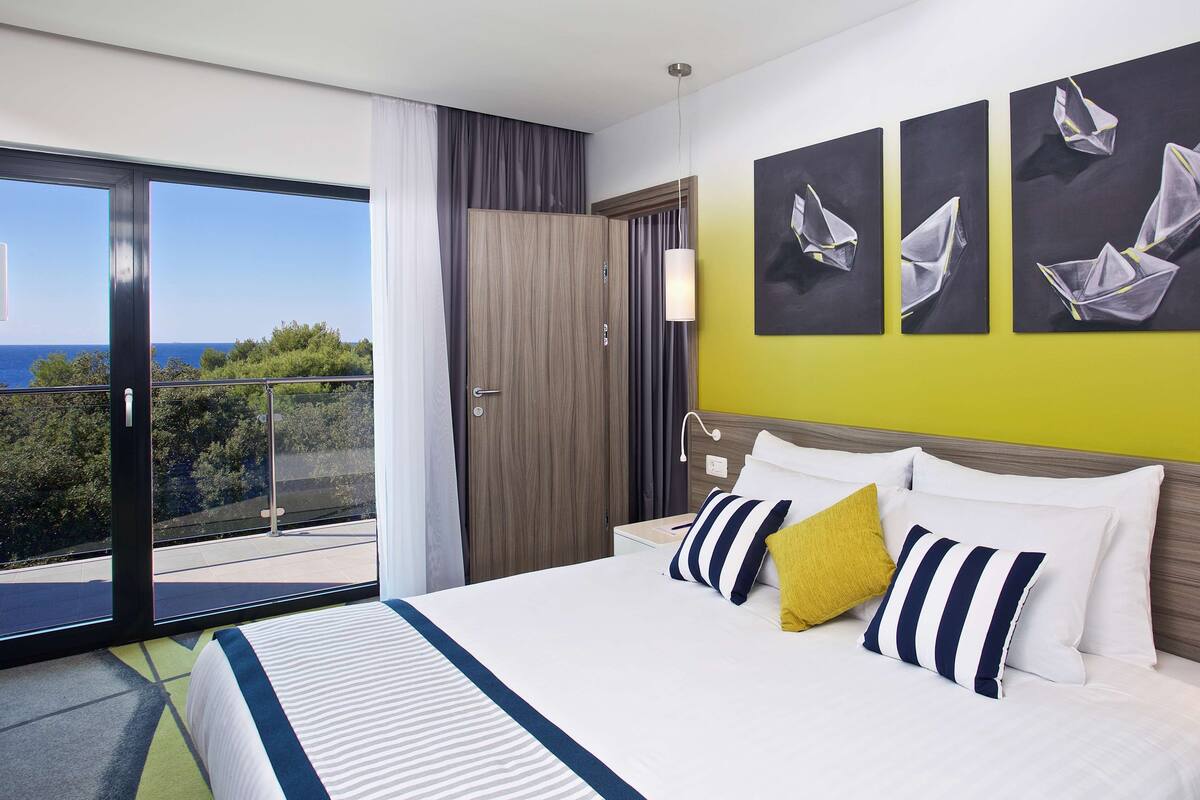 Quarto de hotel com uma cama grande, uma varanda com vista para o mar e três quadros na parede.