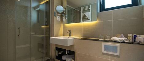 Un baño moderno con ducha de vidrio, lavamanos con espejo y una ventana sobre el espejo.