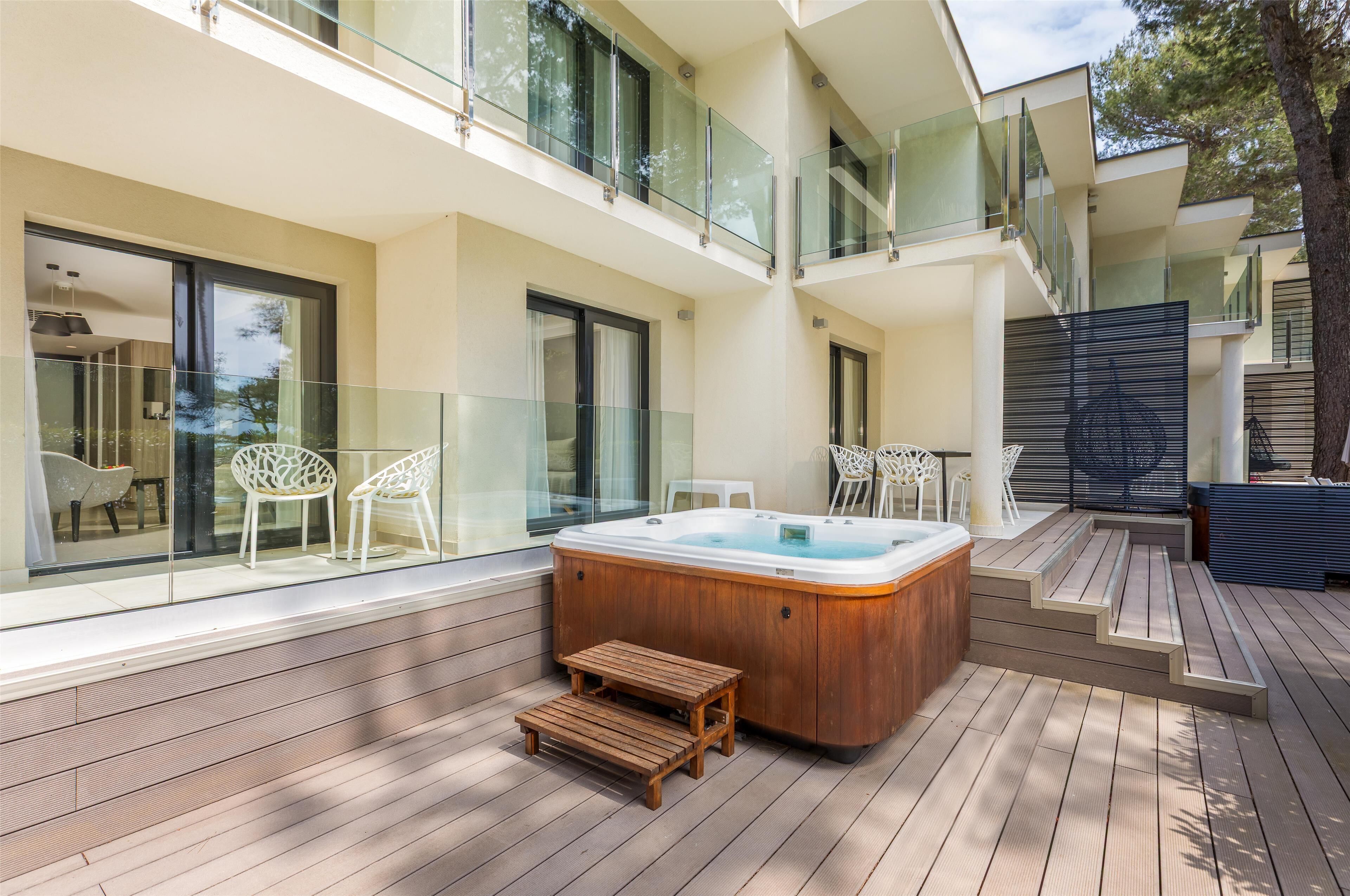 A modern outdoor deck with a hot tub, wooden seating, and glass railings.