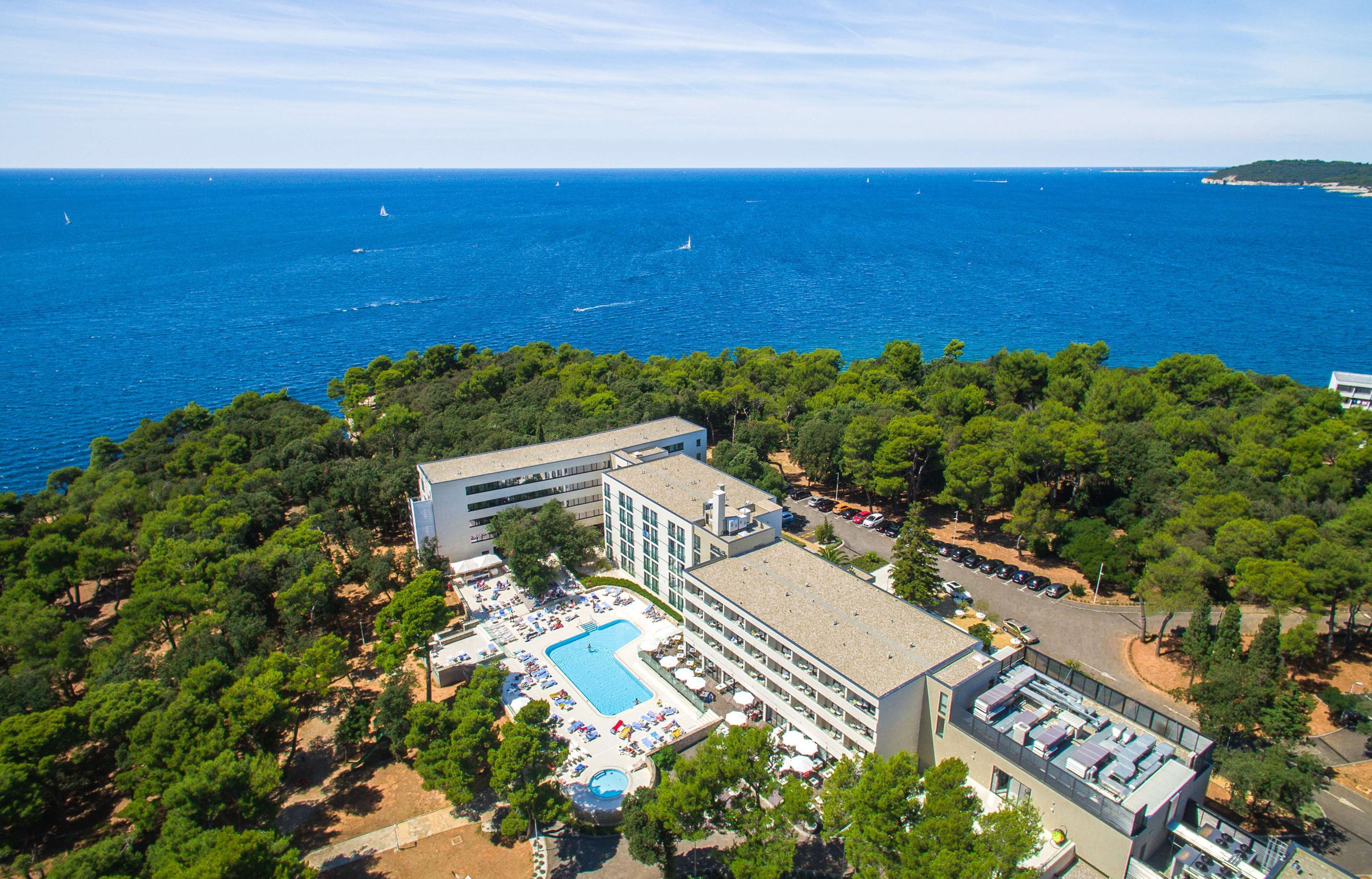 Vista aérea de un hotel costero con piscina, varias edificaciones y vista al mar.