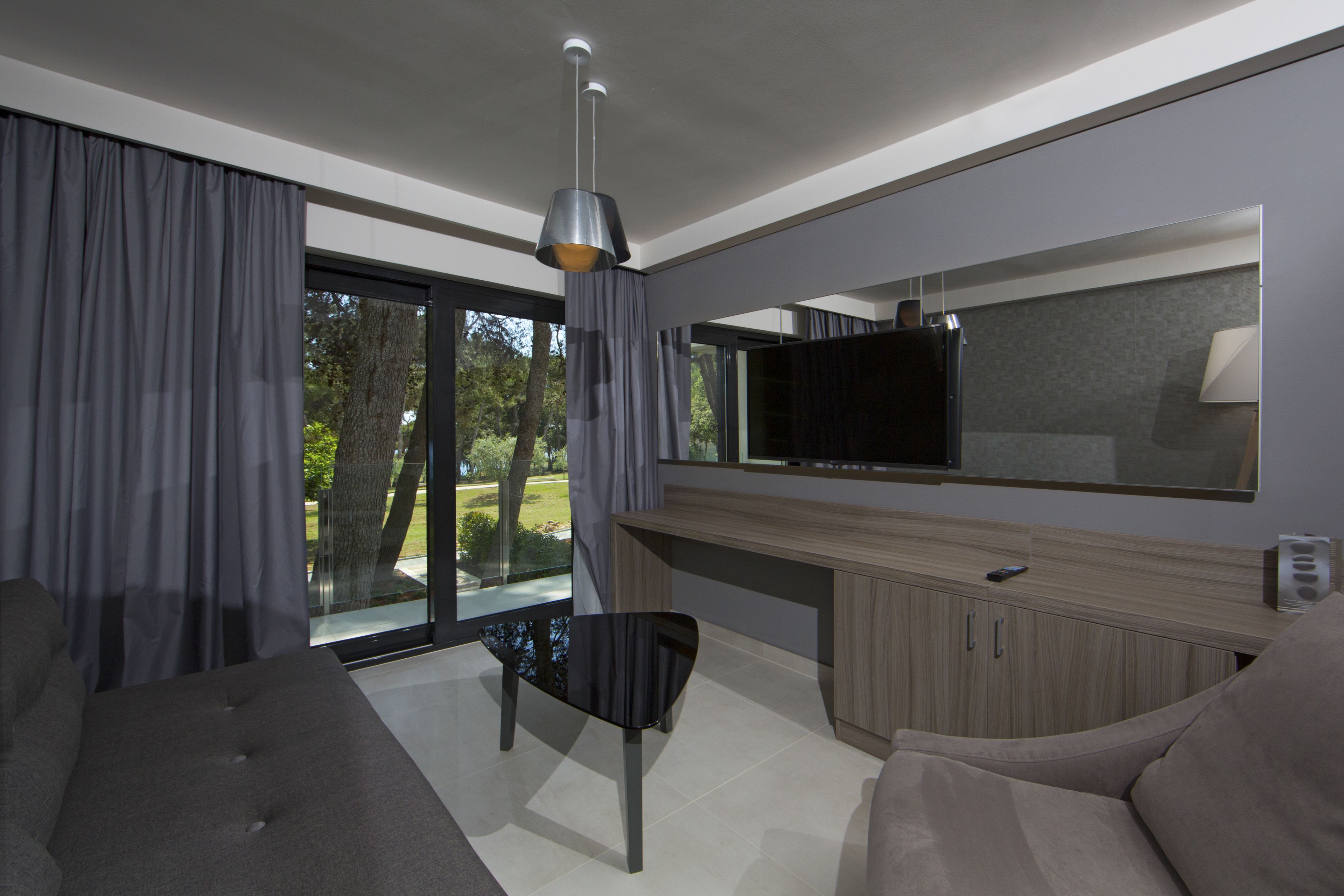 A modern living room with a sofa, a dining table, and a TV mounted on the wall.