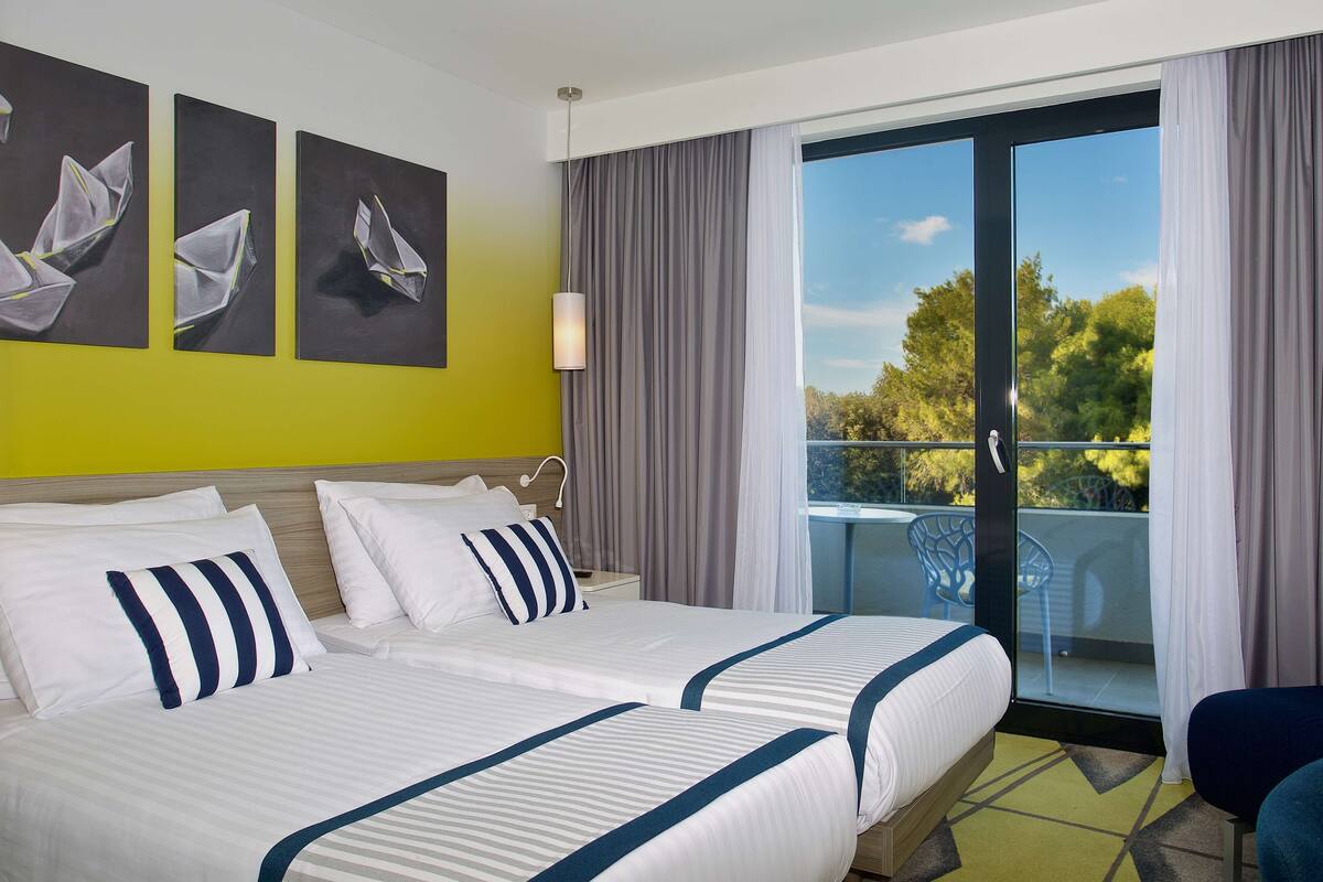 Quarto de hotel com uma cama grande, uma varanda com vista para árvores e obras de arte na parede.