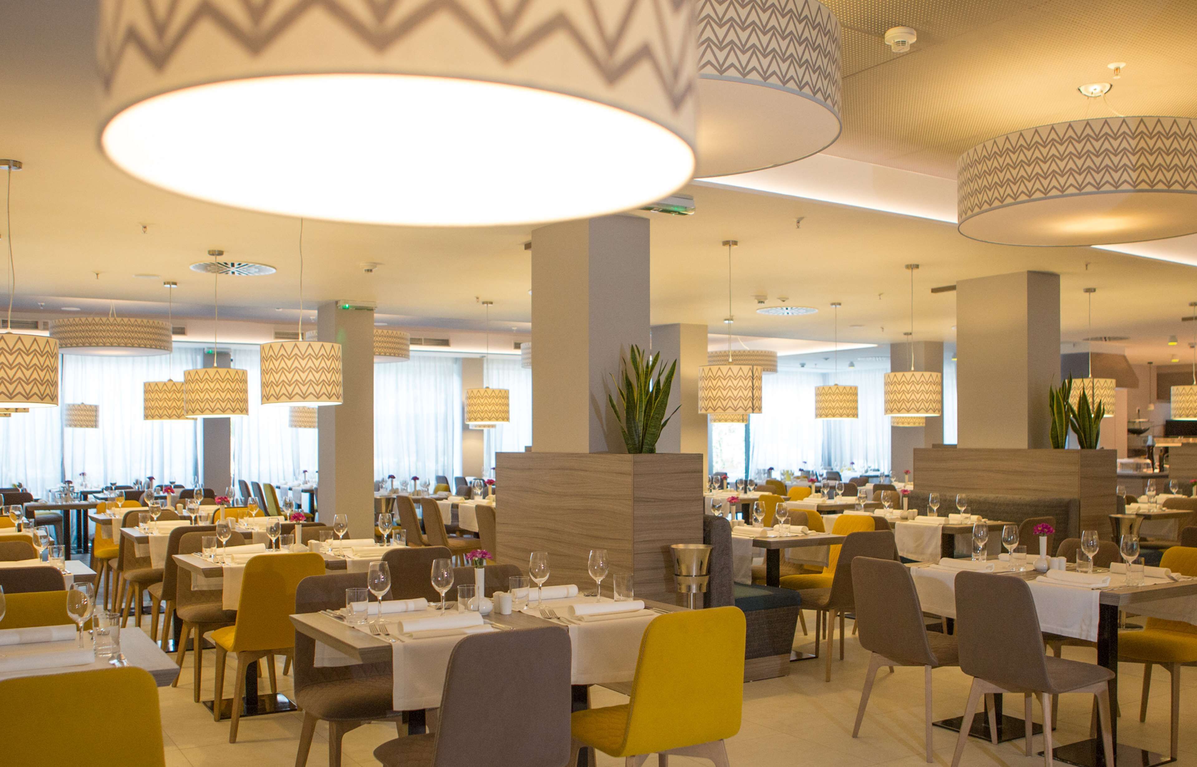 A spacious restaurant with multiple dining tables, yellow chairs, and large hanging lamps.