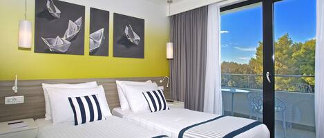 A hotel room with a large bed, a nightstand, a desk, and a balcony with a view of trees.