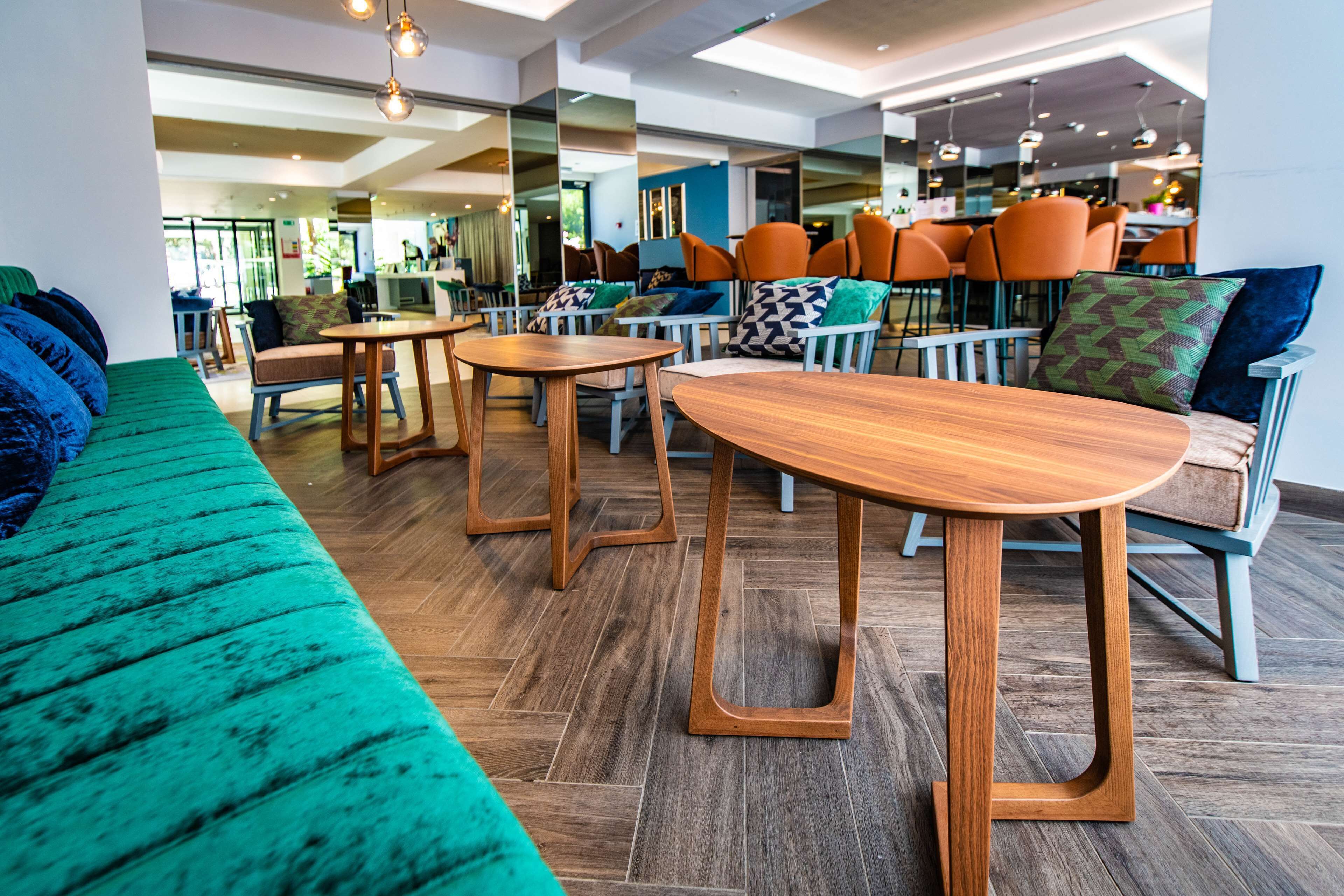 A modern lounge area with a green sofa, wooden tables, and orange chairs.