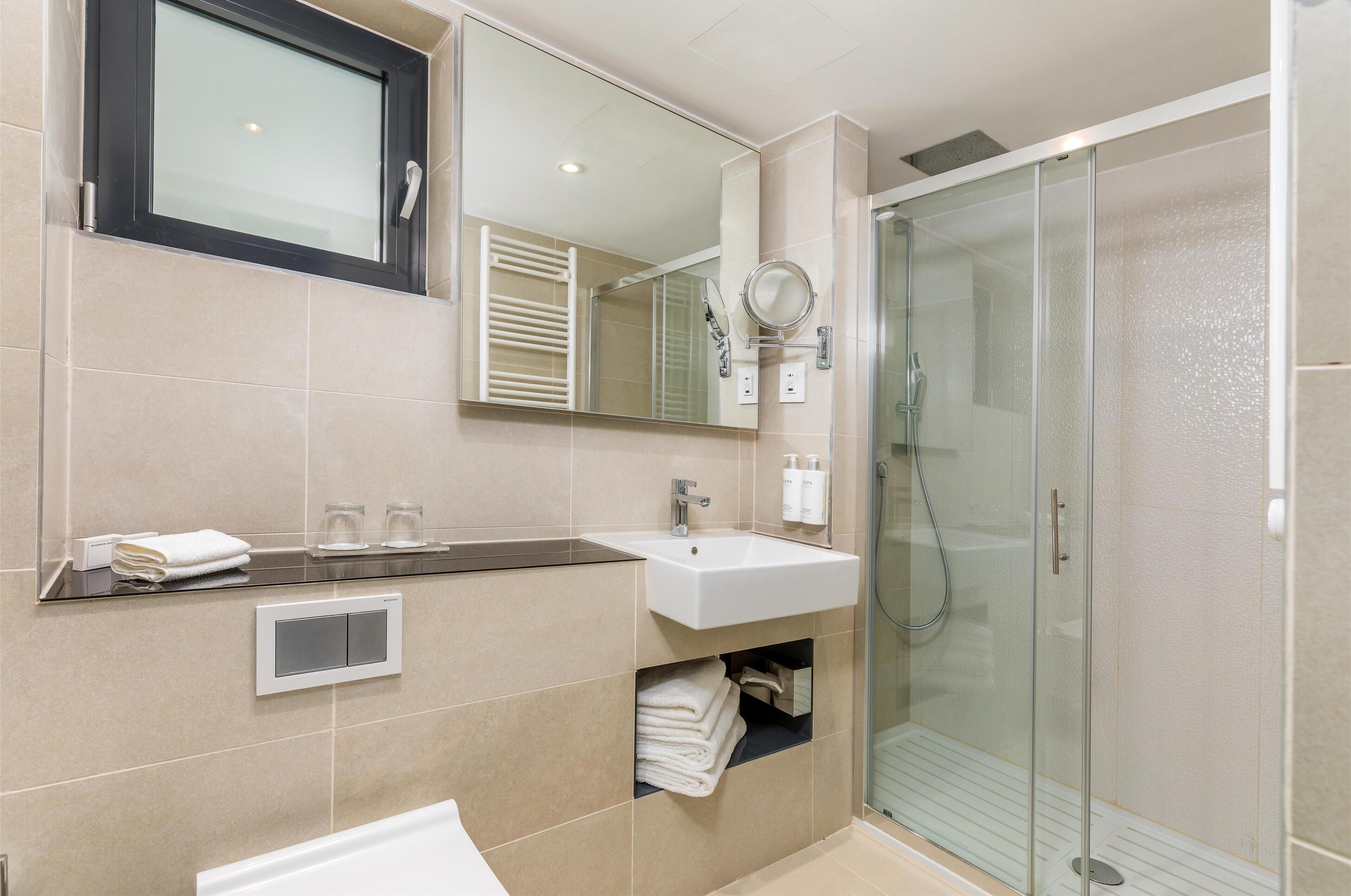 A modern bathroom with a glass-enclosed shower, a white sink, and a large mirror.