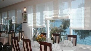 A restaurant with tables set for dining, large windows with curtains, and a view of the sea. - Villa Nova (Neum)