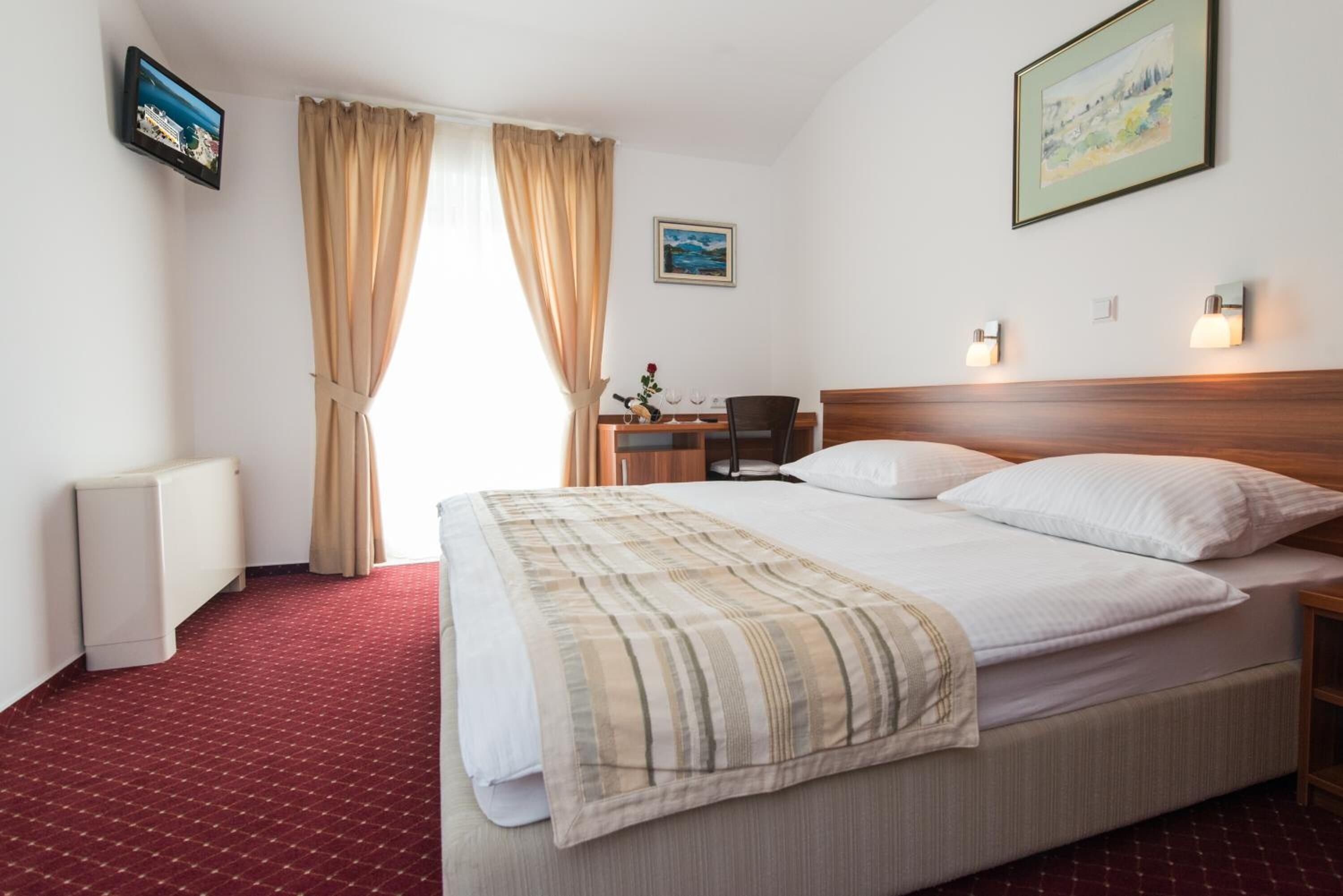 A hotel room with a large bed, a desk with a chair, a radiator, and a television on the wall.