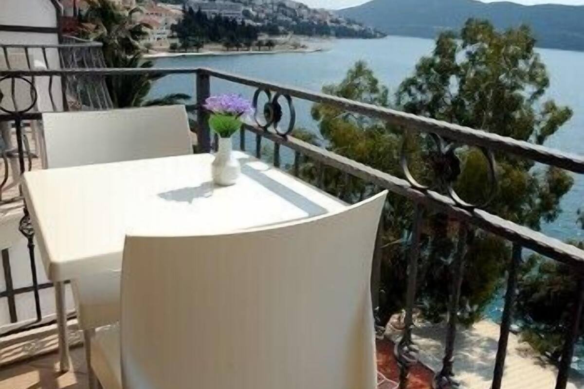 A balcony with a table and chairs, overlooking a body of water and a distant shoreline.