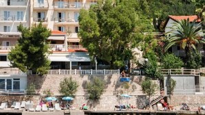 A waterfront hotel with multiple balconies, a swimming pool, and a stone wall. - Villa Nova (Neum)