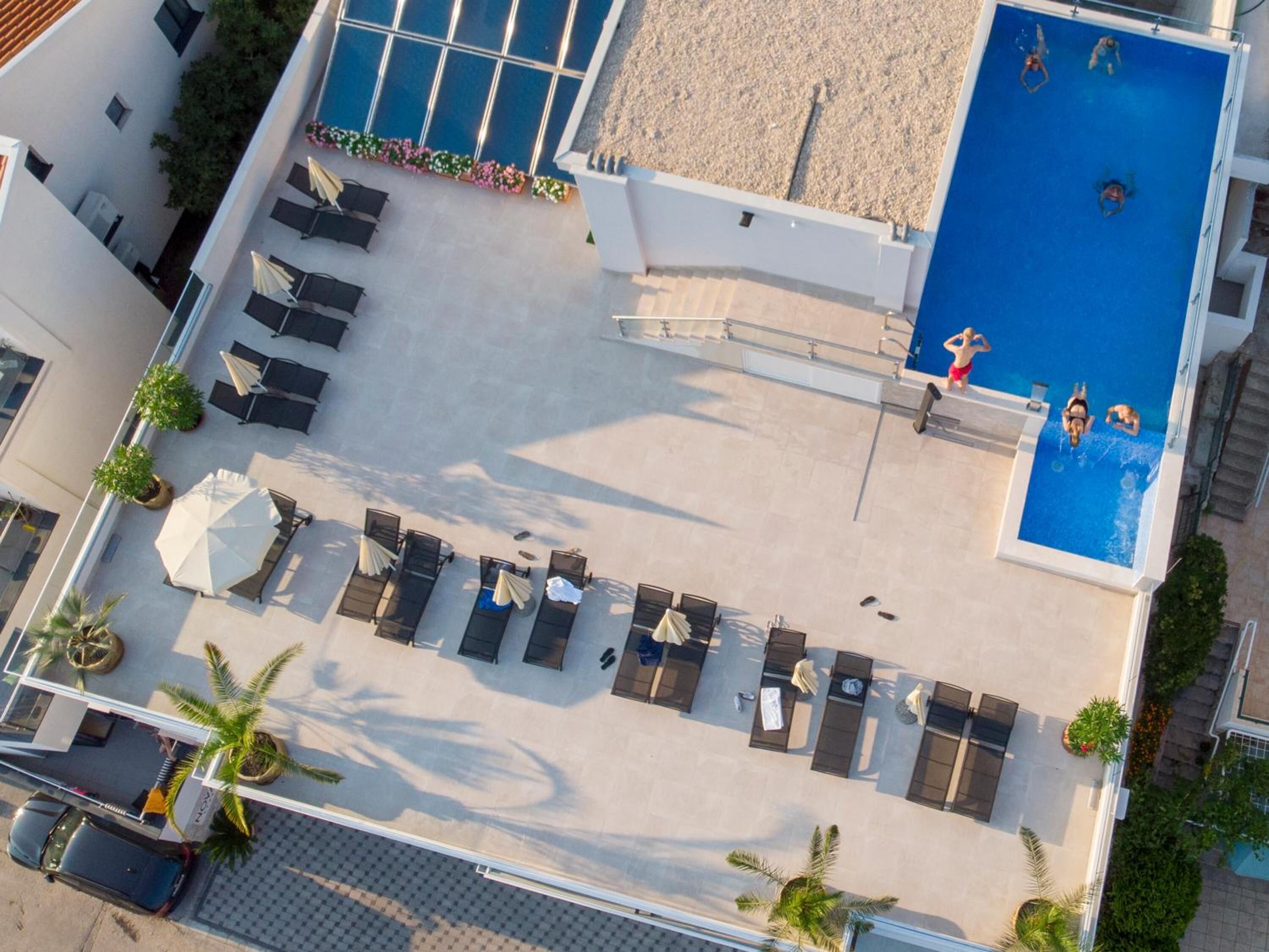 Ein Hotel aus der Vogelperspektive mit Schwimmbecken, Liegestühlen und einer überdachten Außenbereich-Sitzgruppe.