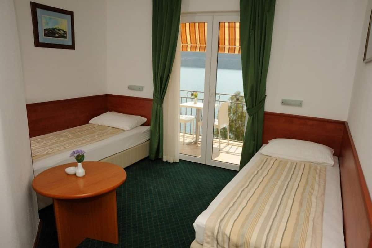 A hotel room with two single beds, a small round table with a vase, and a balcony with a table and chairs.