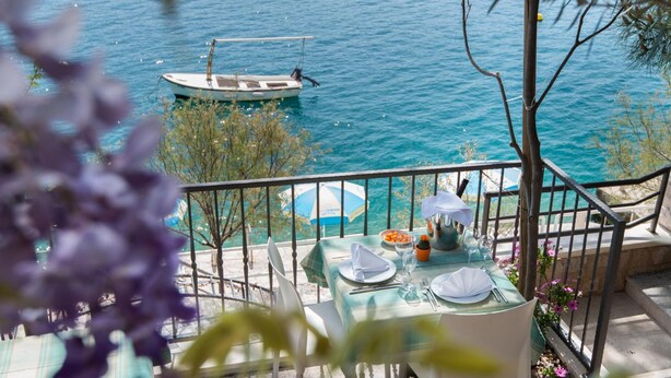 A balcony with a table set for dining, overlooking a body of water with a boat. - Villa Nova (Neum)
