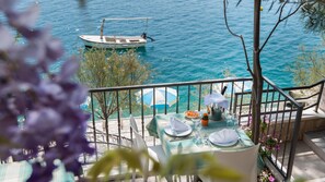 A balcony with a table set for dining, overlooking a body of water with a boat. - Villa Nova (Neum)