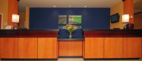 A reception area with a wooden reception desk, a vase with flowers, and a framed artwork on the wall.