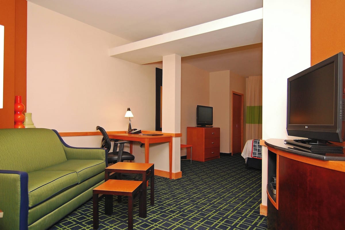 Habitació d'hotel amb un sofà verd, un escriptori de fusta, una televisió i una taula petita.