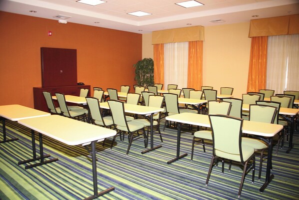 Un salón de conferencias con varias mesas y sillas, una planta grande y una puerta al fondo.