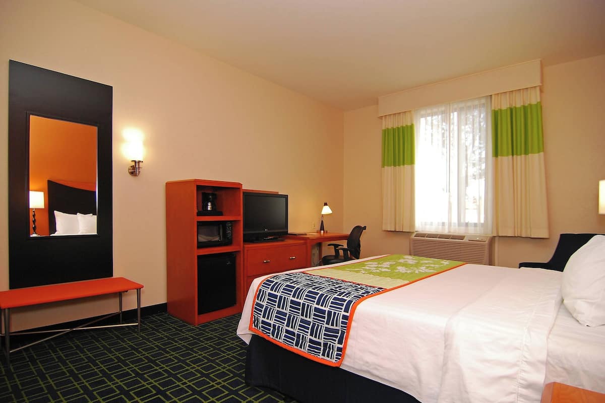 Habitació d'hotel amb un llit, una taula de treball amb un ordinador, una cadira, una panxa i una televisió.