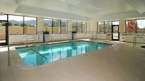 Una piscina interior con vistas claras a montañas a través de amplios ventanales, suelo de baldosas y una escalera de piscina.