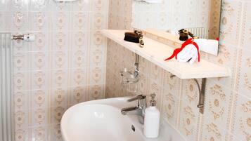 Un baño con papel tapiz estampado, un lavamanos blanco, un espejo y dos toallas en toalleros.