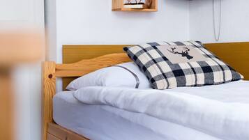 Una cama con cabecera de madera, almohada blanca y almohada con estampado de ciervo a cuadros.