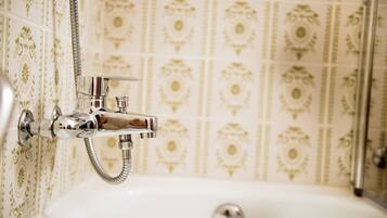 Un bagno con rubinetteria e soffione cromati, una vasca da bagno bianca e carta da parati decorata.