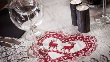 Une table dressée avec un chemin de table en forme de cœur orné d’un motif de cerf, deux bougies et un verre à vin.