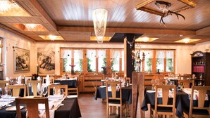 Un restaurant avec des tables et des chaises en bois, des lustres et des œuvres d’art accrochées aux murs.