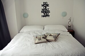 A neatly made bed with white linens and two decorative pillows, a wall with a motivational quote, and a small table with a decorative item. - Hotel Marmotte (Saas-Fee)