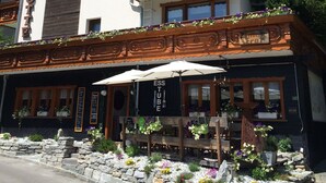 Un hôtel à plusieurs étages doté de balcons ornés de fleurs, d’une façade en pierre et d’un espace extérieur aménagé avec des parasols.
