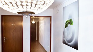 Un couloir avec une porte en bois portant le numéro « 42 », un lustre moderne et une œuvre d’art murale représentant une feuille de basilic.