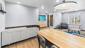 Une cuisine moderne avec des meubles blancs, une table à manger en bois et un luminaire suspendu.