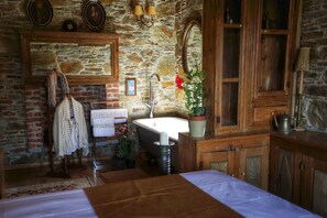 Un baño rústico con pared de piedra, armarios de madera, un lavamanos blanco y una bañera.