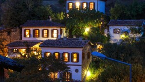 A cluster of traditional buildings with multiple windows, surrounded by greenery, and illuminated by street lamps. - Terrace Houses Sirince - Fig, Olive Clockmakers and Grapevine (Selçuk)