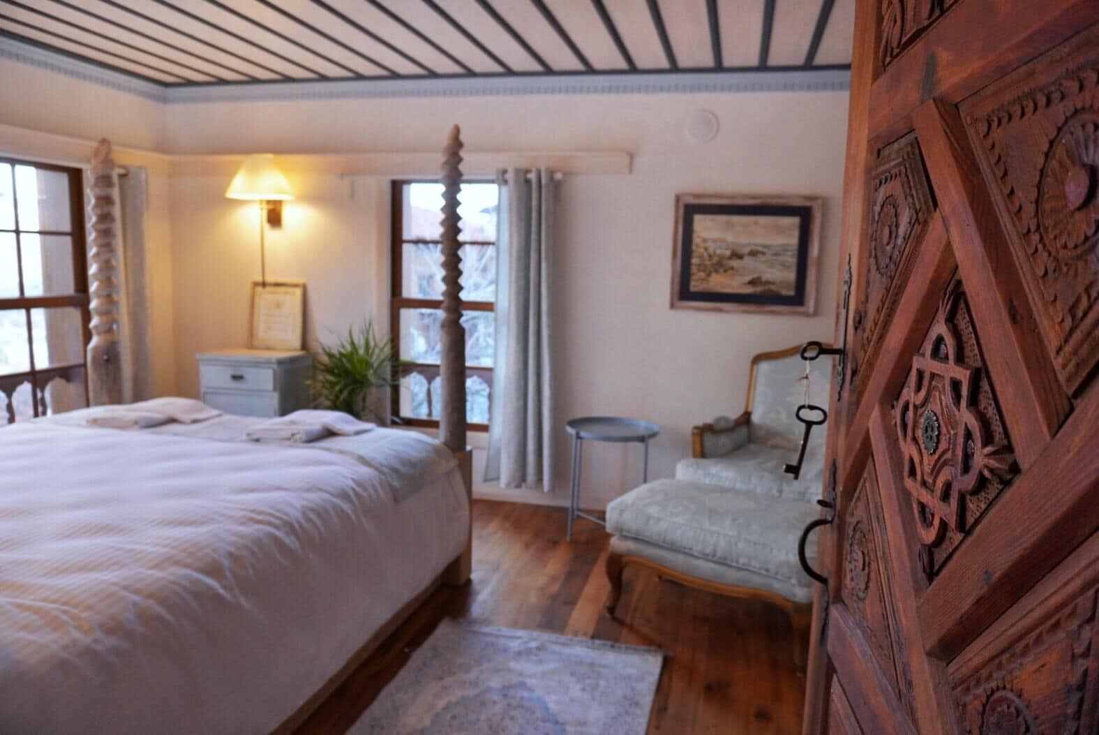 A bedroom with a large bed, a chair, a small table, a lamp, and a painting on the wall.