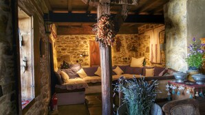 A rustic room with a stone wall, wooden beams, a wooden cross, a sofa with cushions, a table with a plant, and a window with a view. - Terrace Houses Sirince - Fig, Olive Clockmakers and Grapevine (Selçuk)