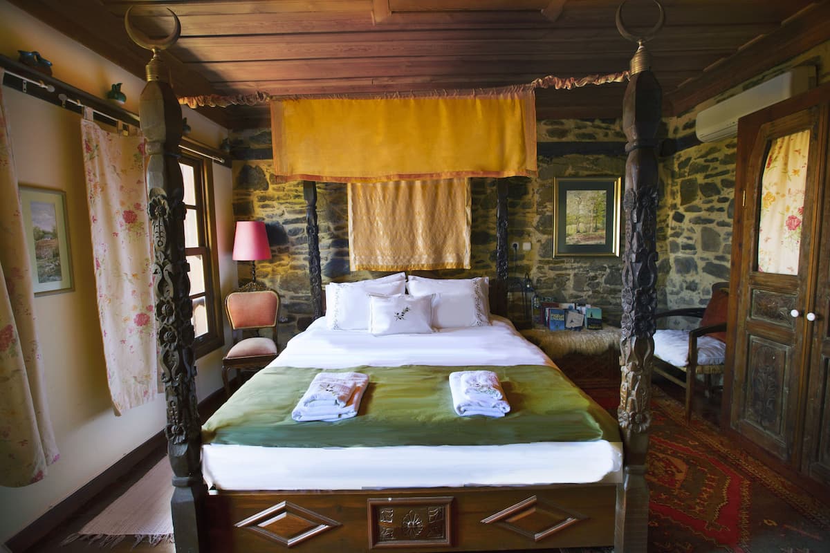 A four-poster bed with a canopy, a stone wall, and a wooden floor.