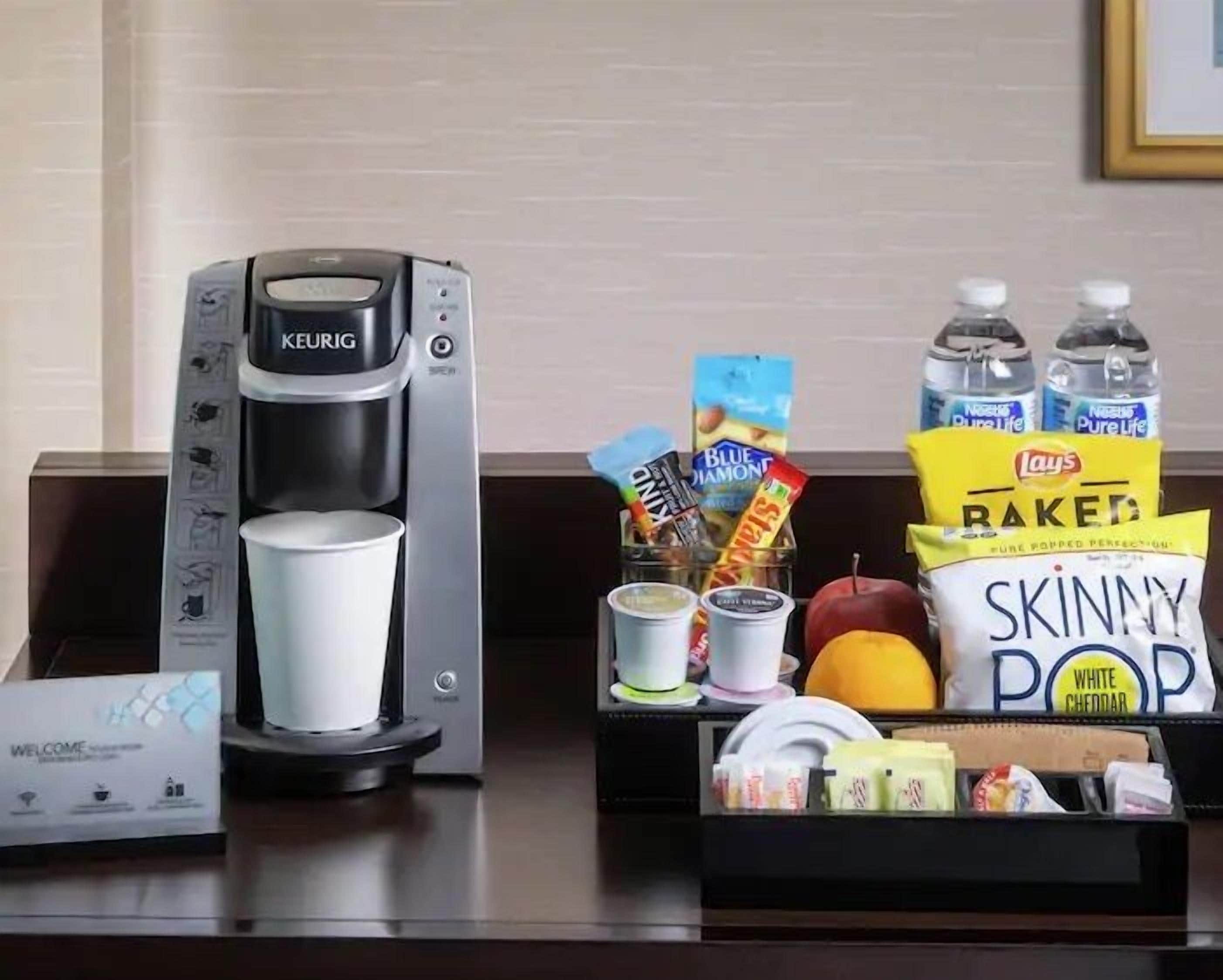 A coffee maker, a cup, snacks, and bottled water on a hotel reception desk.