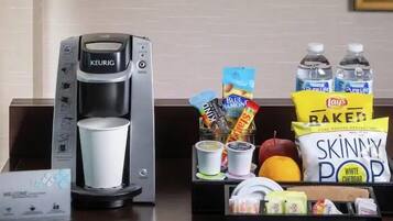 A coffee maker, a cup, snacks, and bottled water on a hotel reception desk.
